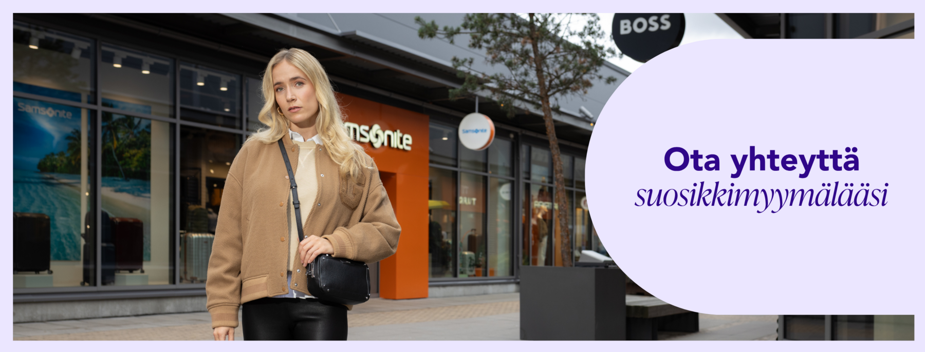 Beigeen GANT-takkiin pukeutunut nainen seisoo Helsinki Outletissa Samsonite- ja BOSS-myymälöiden edessä.