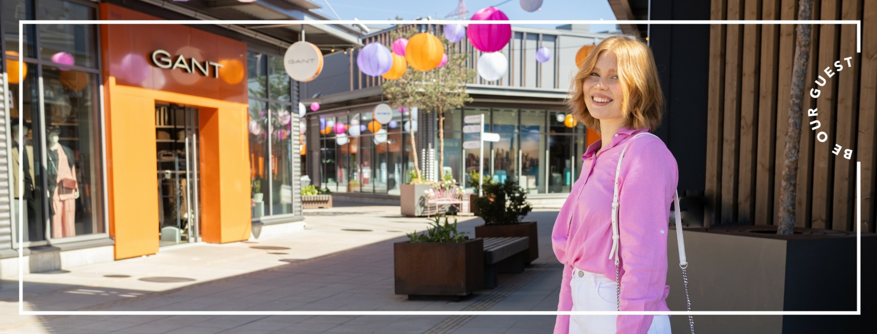 A woman with red hair and a pink shirt standing at the entrance of a shopping village
