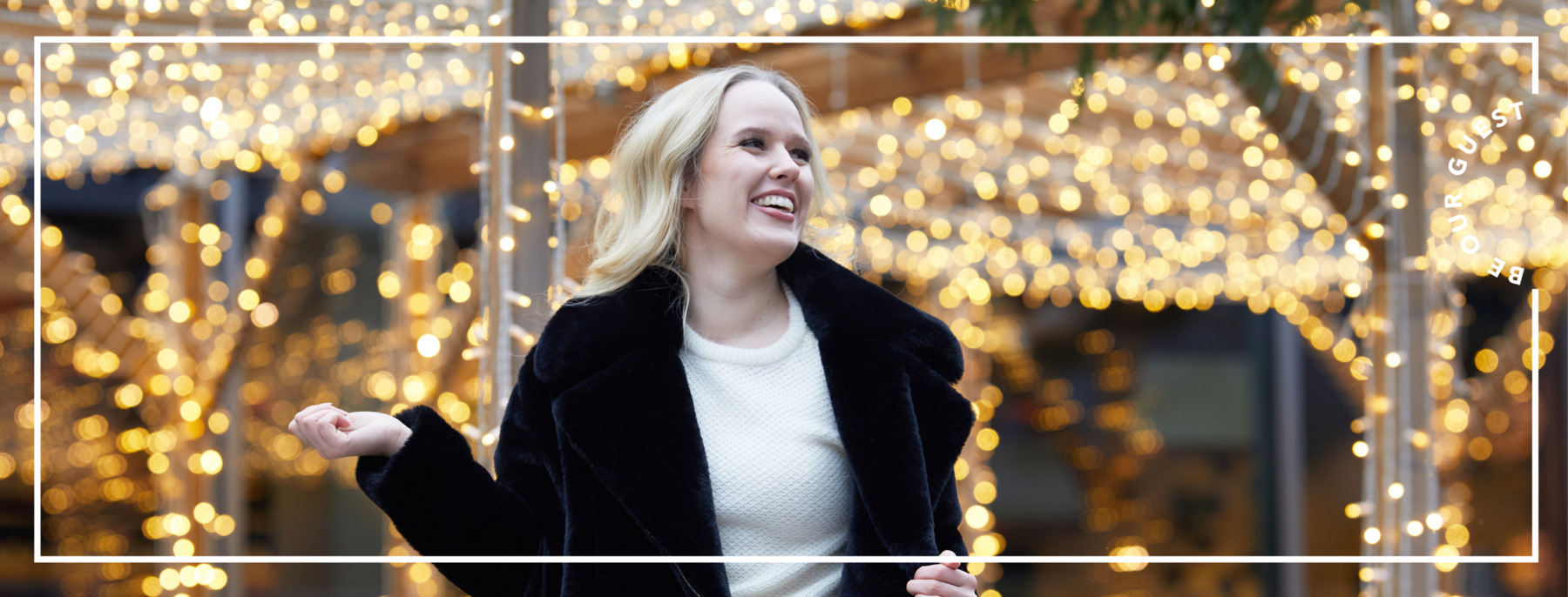 A woman smiling in the shopping village beside her beautiful Christmas lights